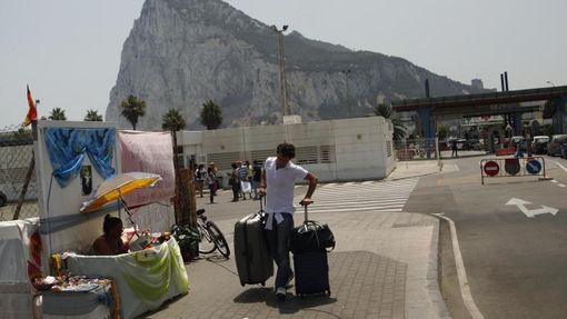Muž odnáší kufry, právě opustil britské území Gibraltaru. V pozadí je vidět část gibraltarské skály - monolitického vápencového ostrohu.