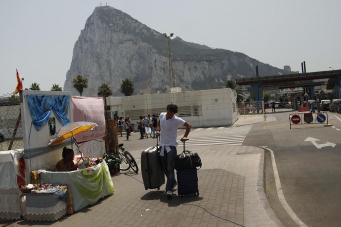 Muž odnáší kufry, právě opustil britské území Gibraltaru. V pozadí je vidět část gibraltarské skály - monolitického vápencového ostrohu.