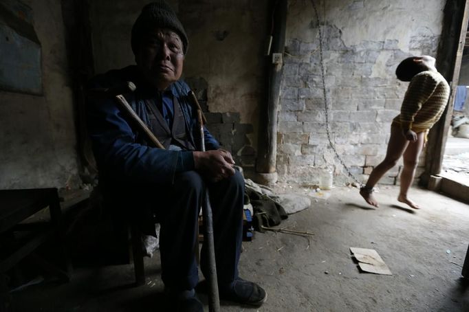 A boy is seen chained to a wall as his grandfather sits next to him at their home in Zhejiang province