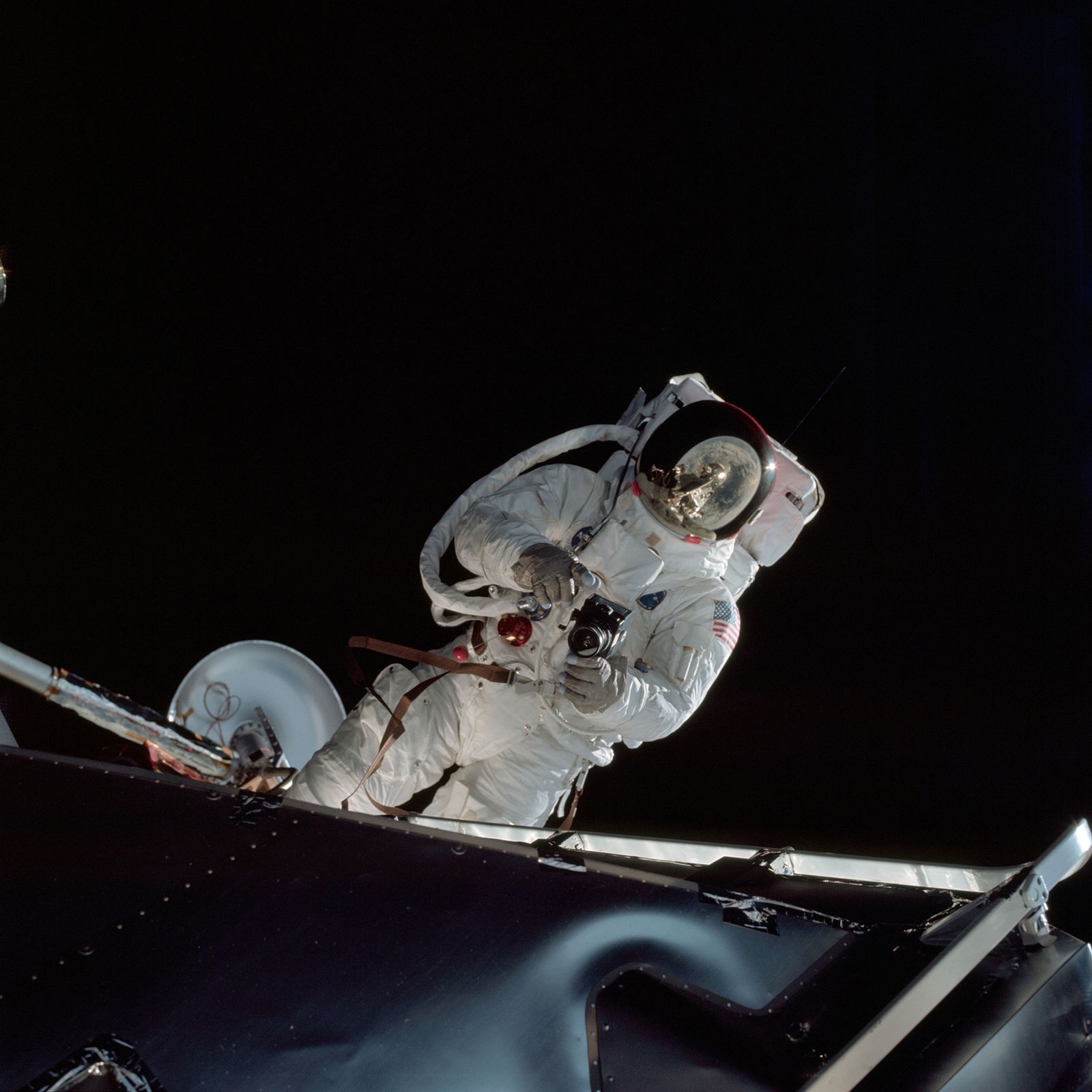 Astronaut Russell L. Schweickart drží v rukou fotoaparát během výstupu do volného vesmíru. Snímek je z mise Apollo 9 (1969)