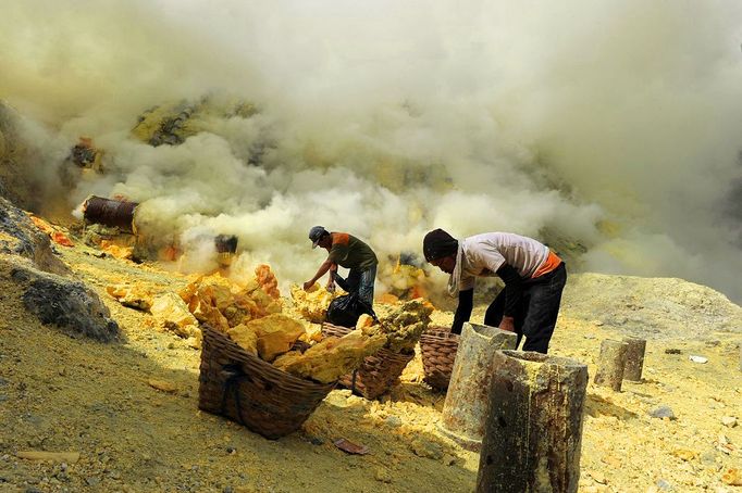 This photo taken on December 25, 2010 shows Indonesian miners filling baskets with sulphur before carrying them from the bottom of the crater of Indonesia's active Kajah Iwen volcano, in the extreme east of Java island. Some 350 sulphur miners eke out a dangerous and exhausting living on the active volcano, carrying hauls of up to 80 kilos of "yellow gold" which will be bought by local factories and used to refine sugar or make matches and medicines. The miners extract the liquid sulphur as it flows out of hot iron pipes. Once in the open air, it cools, crystallises and turns bright yellow. The sulphur is then loaded into wicker baskets at either end of bamboo yokes and carried back over the lip of the crater and down the side of the volcano, a treacherous journey of four kilometres (2.5 miles).