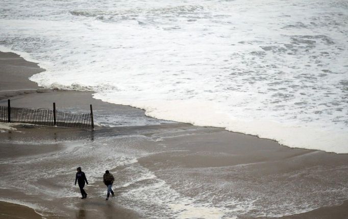 People walk near a surf from Hurricane Sandy rising past sand fences onto the beach in Ocean City, Maryland October 28, 2012. Tens of millions of East Coast residents scrambled on Sunday to prepare for Hurricane Sandy, which could make landfall as the largest storm to hit the United States, bringing battering winds, flooding and even heavy snow. REUTERS/Kevin Lamarque (UNITED STATES - Tags: ENVIRONMENT DISASTER)