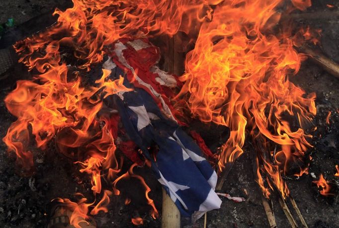 A burning U.S. flag is seen on the ground after it was set on fire by Bangladeshi Muslims during a protest in front of the National Press Club in Dhaka September 21, 2012. About 10,000 Bangladeshi Muslims participated in demonstrations after Friday prayers in Bangladesh's capital against an anti-Islam film made in the U.S. and also against cartoons mocking the Prophet Mohammad published on Wednesday in a French magazine. REUTERS/Andrew Biraj (BANGLADESH - Tags: RELIGION POLITICS CIVIL UNREST) Published: Zář. 21, 2012, 11:09 dop.