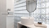Nejvýraznějším prvkem interiéru je zaoblená stěna z luxfer, která propouští denní světlo do koupelny, ale zároveň poskytuje dostatek soukromí.