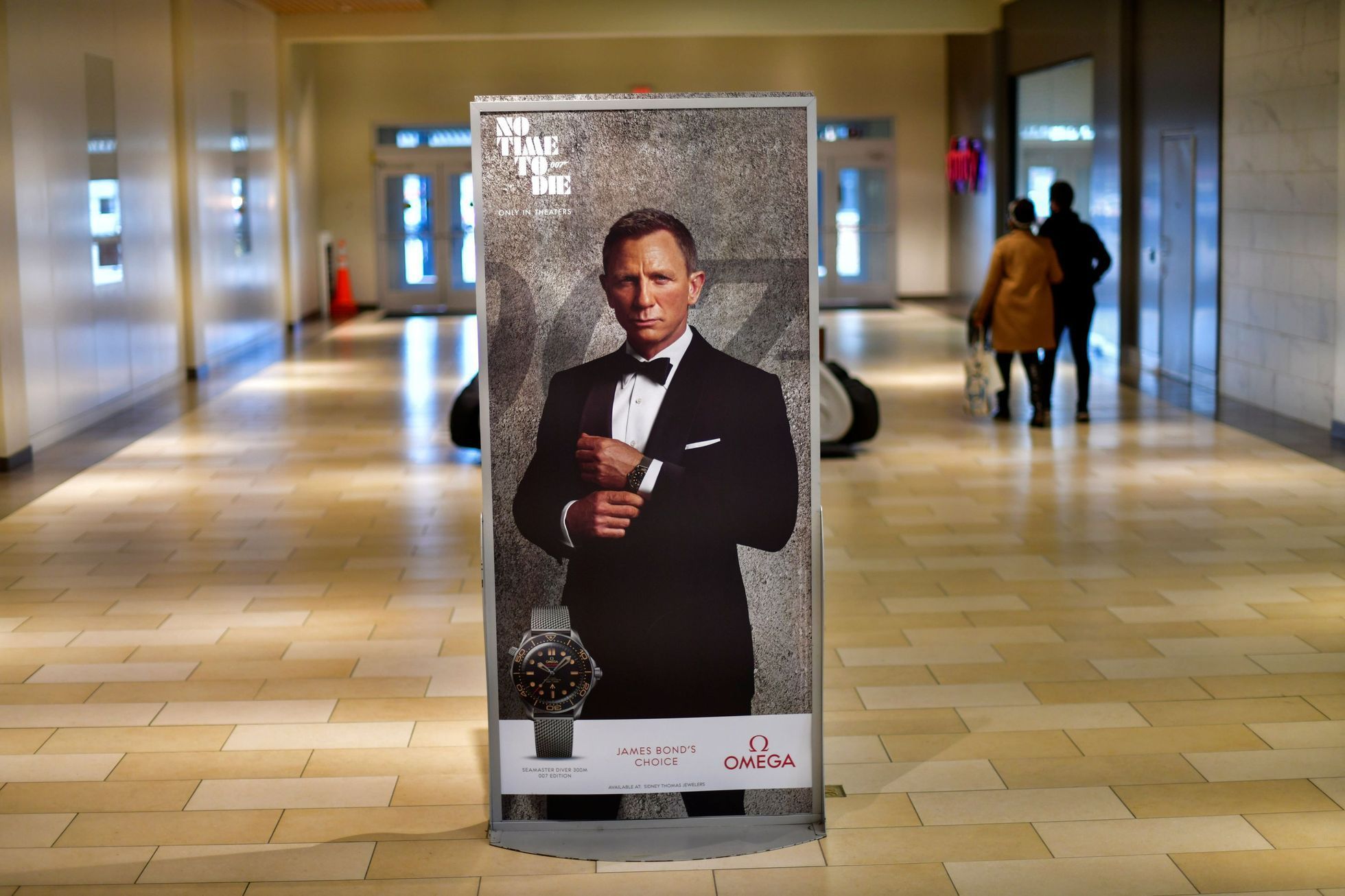 Shoppers walk past an advertisement for the upcoming James Bond film "NO TIME TO DIE" whose release has been delayed due to the coronavirus disease (COVID-19) pandemic at the Christiana Mall in Newark