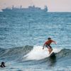 A surfer catches a wave with a navy ship behind him, Tuesday, Sept. 11, 2018, in Virginia Beach, Va., before the arrival of Hurricane Florence.