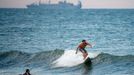 A surfer catches a wave with a navy ship behind him, Tuesday, Sept. 11, 2018, in Virginia Beach, Va., before the arrival of Hurricane Florence.