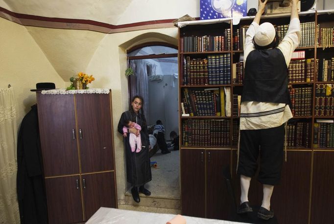 Yoel Kreus (R) reaches for a box as his daughter Esther, 13, holds her 3-week old sister during the family's preparations for the Jewish Sabbath in Jerusalem's Mea Shearim neighbourhood June 29, 2012.The Kreus family are a member of Neturei Karta, a fringe ultra-Orthodox movement within the anti-Zionist bloc. The ultra-Orthodox Jews have gone from being a tiny minority in Israel's mostly secular society to its fastest-growing sector, now about 10 percent of the 7.8 million population. They are exempt from military duty in Israel but draft deferments and state subsidies for the ultra-Orthodox have become a divisive political issue in Israel, where the government must decide a new law by August to ensure more of them do military service. Picture taken June 29, 2012. REUTERS/Ronen Zvulun (JERUSALEM - Tags: RELIGION POLITICS MILITARY) ATTENTION EDITORS - PICTURE 8 OF 21 FOR PACKAGE "ISRAEL'S ULTRA-ORTHODOX". SEARCH "ULTRA-ORTHODOX" FOR ALL PICTURES Published: Čec. 6, 2012, 10:01 dop.