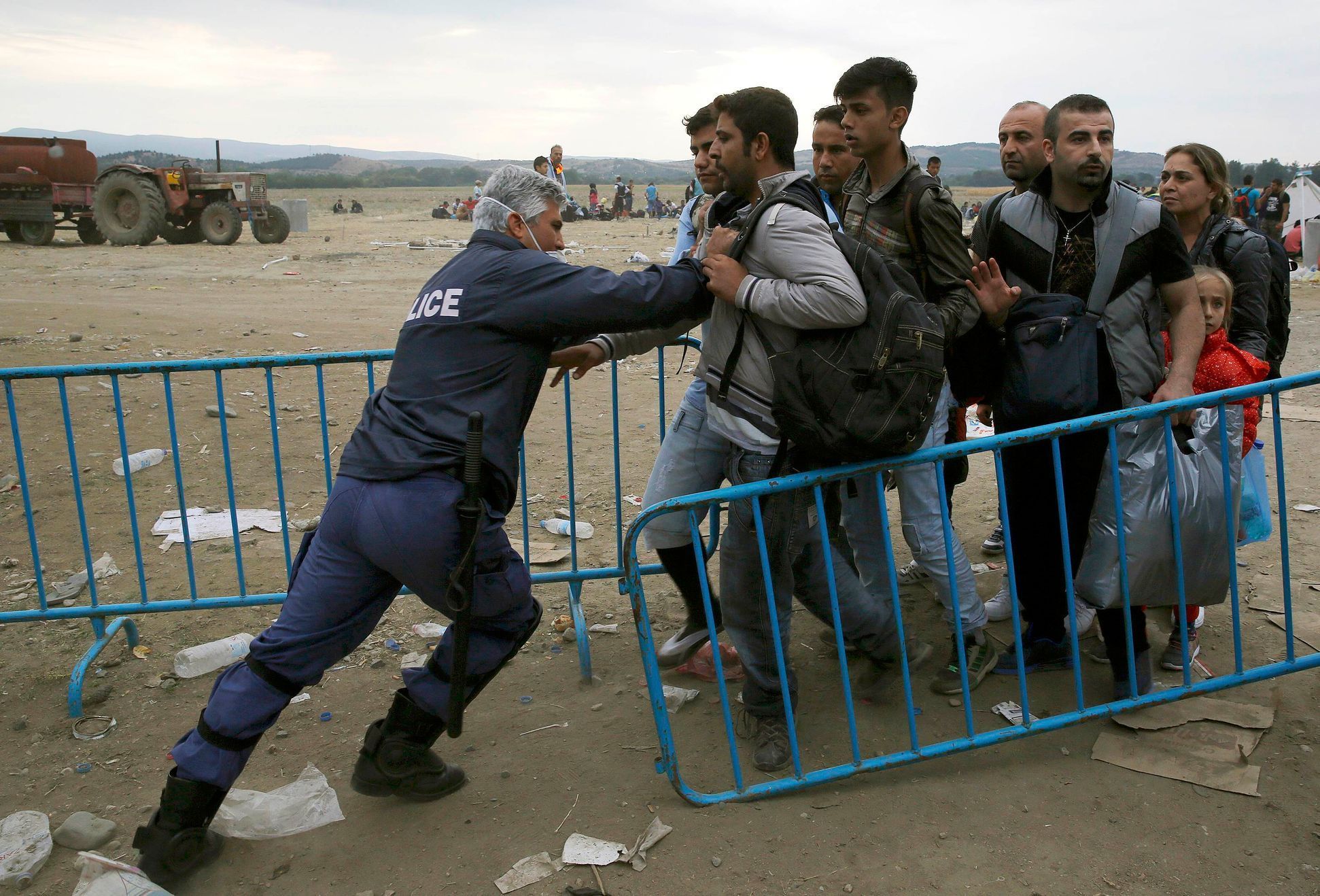 Řecký policista tlačí uprchlíky zpět za bariéru.