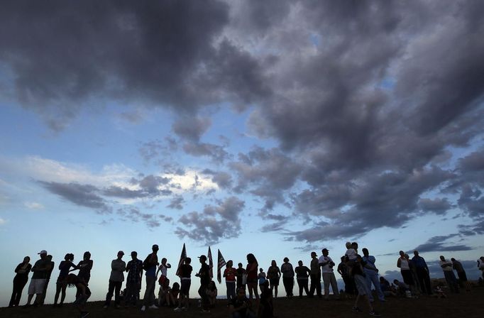 People stand on a hillside behind a memorial for victims behind the theater where a gunman opened fire on moviegoers in Aurora, Colorado July 22, 2012. Residents of a Denver suburb mourned their dead on Sunday from a shooting rampage by a "demonic" gunman who killed 12 people and wounded 58 after opening fire at a cinema showing the new Batman movie. REUTERS/Shannon Stapleton (UNITED STATES - Tags: DISASTER SOCIETY CIVIL UNREST CRIME LAW) Published: Čec. 23, 2012, 2:32 dop.