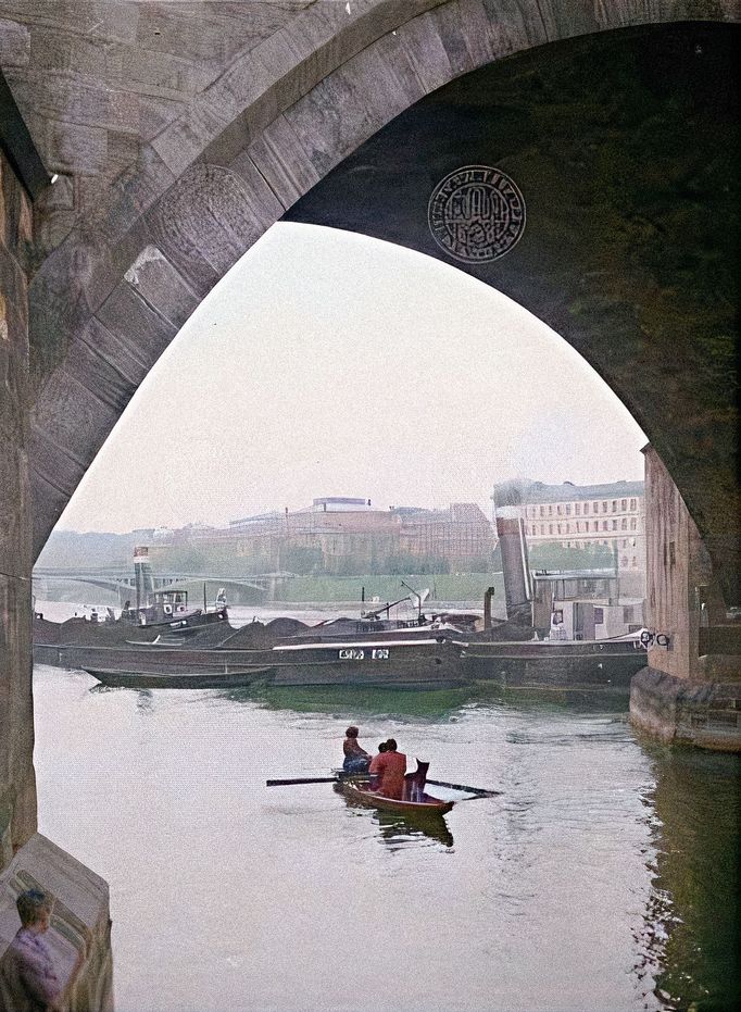 Pohled na Vltavu s nákladními parníky s uhlím u Karlova mostu. V pozadí Palachovo náměstí a část Mánesova mostu. Rok 1958. Kolorováno