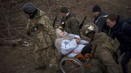 Ukrajinští vojáci a milicionáři nesou ženu na invalidním vozíku během evakuace civilistů z předměstí Kyjeva. 7. 3. 2022