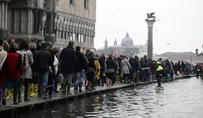 Tourists walk on raised platforms for flood waters in St. Mark Square during a period of seasonal high water in Venice October 27, 2012. The water level in the canal city rose to 127 cm (50 inches) above the normal level, according to the monitoring institute. REUTERS/Manuel Silvestri (ITALY - Tags: ENVIRONMENT SOCIETY TRAVEL) Published: Říj. 27, 2012, 11:52 dop.