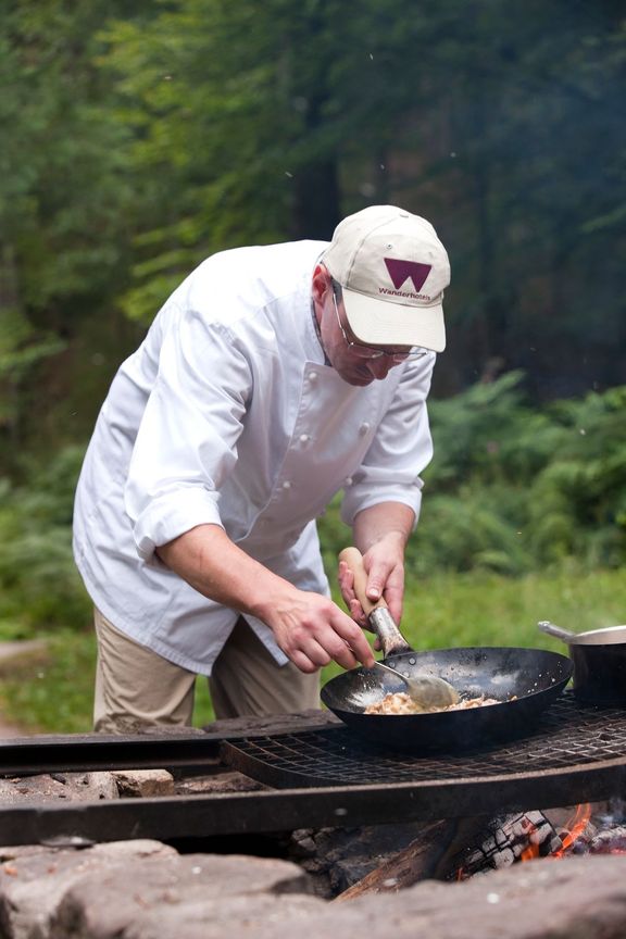 Wanderhotels - kuchař připravuje pokrm na otevřeném ohni