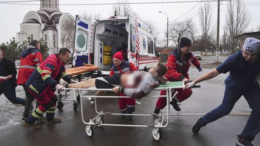Zdravotníci přemísťují muže na nosítkách zraněného ostřelováním v obytné čtvrti. Mariupol, 1. 3. 2022