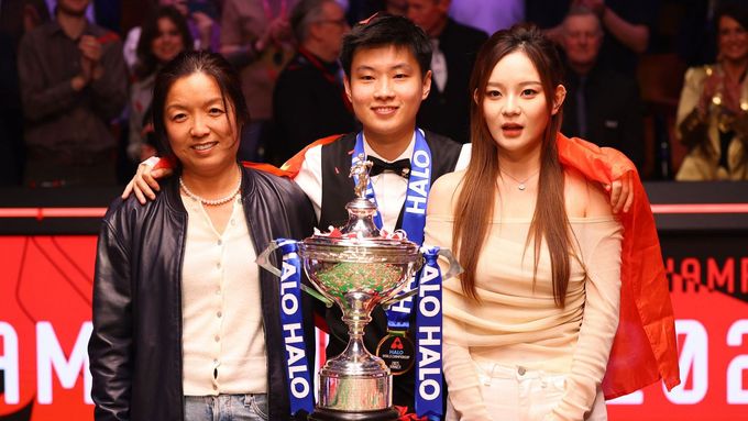Čao Sin-tchung pózuje s trofejí pro mistra světa a svou manažerkou a partnerkou