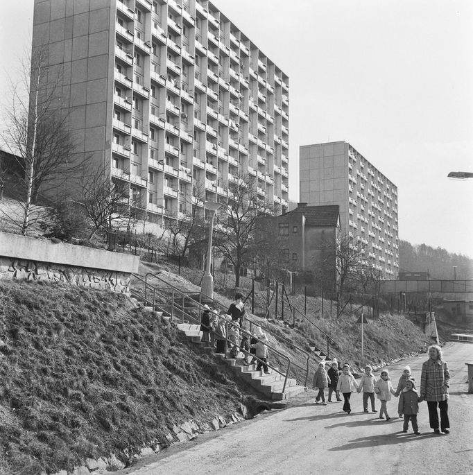 Děti z mateřské školky v doprovodu učitelek kráčí okolo tehdy nově postavených panelových domů v Adamově, rok 1975.