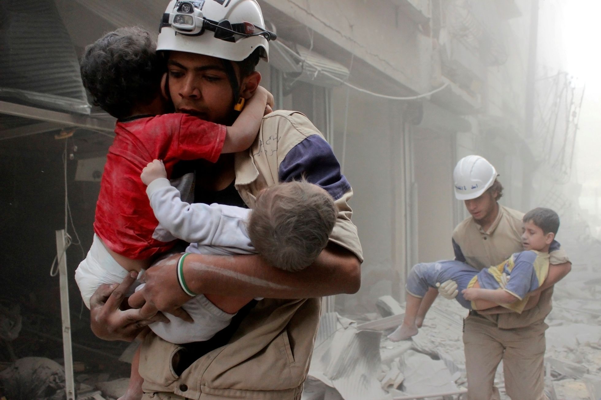 Záchranáři vynášejí děti z rozbombardovaných domů ve východním Aleppu.