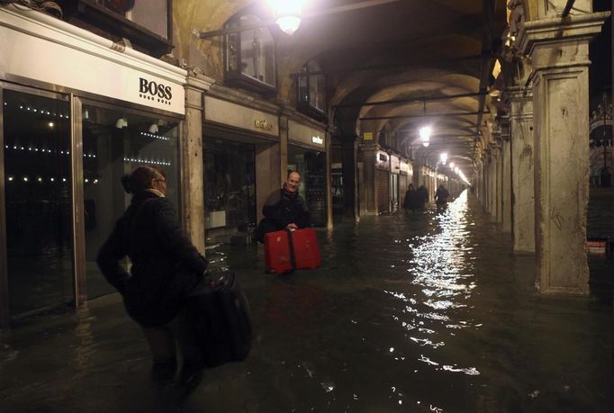 People carry their luggage in a flooded St Mark's Square at night during a period of seasonal high water in Venice November 1, 2012. The water level in the canal city rose to 140 cm (55 inches) above normal, according to the monitoring institute. REUTERS/Manuel Silvestri (ITALY - Tags: ENVIRONMENT SOCIETY TRAVEL DISASTER) Published: Lis. 1, 2012, 8:33 dop.