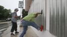 Simone Haug (L) looks on as Mary Piszker kicks a section into place as they work on the finishing touches on a window shutter installation in front of a clinic named "Womankind", in preparation for the arrival of Tropical Storm Isaac in Key West, FL August 25, 2012, where the storm's maximum effect is expected tomorrow. REUTERS/Andrew Innerarity (UNITED STATES - Tags: ENVIRONMENT DISASTER) Published: Srp. 25, 2012, 9:29 odp.