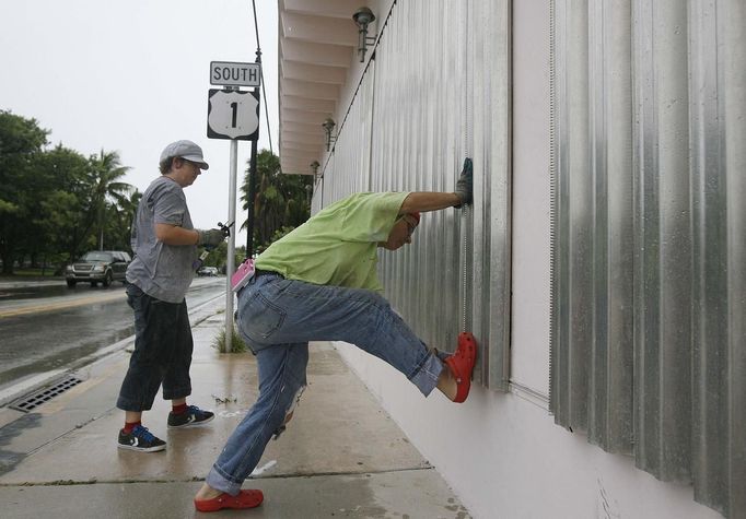 Simone Haug (L) looks on as Mary Piszker kicks a section into place as they work on the finishing touches on a window shutter installation in front of a clinic named "Womankind", in preparation for the arrival of Tropical Storm Isaac in Key West, FL August 25, 2012, where the storm's maximum effect is expected tomorrow. REUTERS/Andrew Innerarity (UNITED STATES - Tags: ENVIRONMENT DISASTER) Published: Srp. 25, 2012, 9:29 odp.