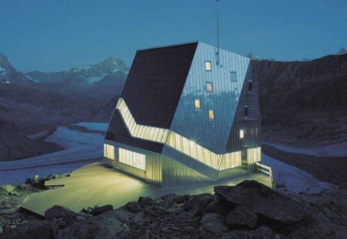 Nová chata Monte Rosa (noční pohled), Valentin Bearth, Andrea Deplazes, Daniel Ladner/ Bearth & Deplazes Architekten AG; ETH-ZURICH/ Studio Monte Rosa, Zermatt, 2009  V extrémních alpských podmínkách vypadá nová chata Monte Rosa jako kamenný krystal s velmi malým dopadem na životní prostředí díky využití průkopnických technologií, které pracují se zdroji efektivně a omezují spotřebu energie na absolutní minimum.