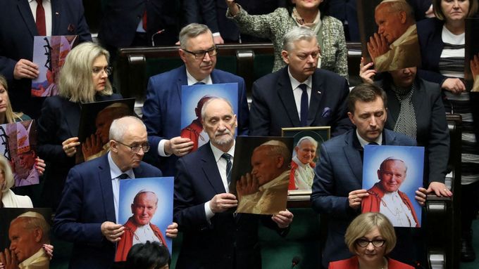 Zákonodárci z Práva a spravedlnosti drží v rukou podobizny papeže během debaty o rezoluci na obranu jména Jana Pavla II. v parlamentu.