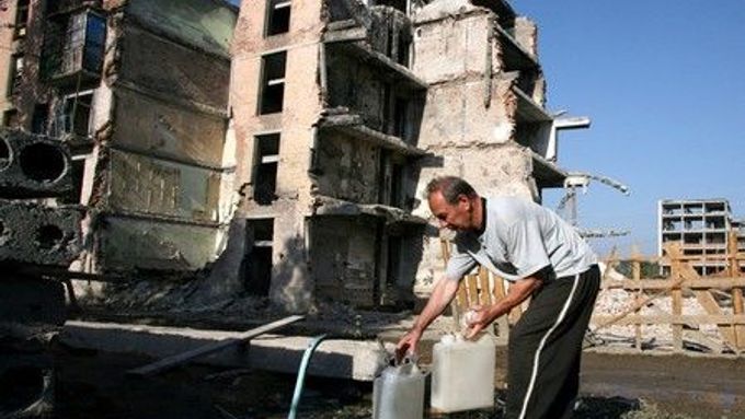 Muž plní kanystr před zničeným panelovým domem v Grozném.
