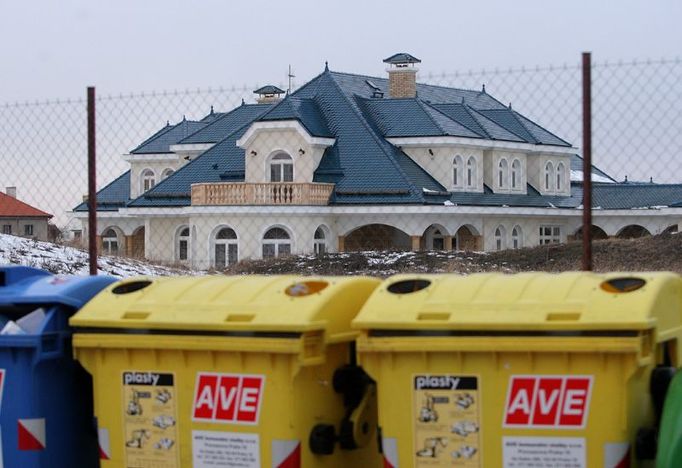 Rozlehlý dům neskryje ani hradba kontejnerů na tříděný odpad, ani dvoumetrový val ze zeminy. Pohled od jihovýchodu.