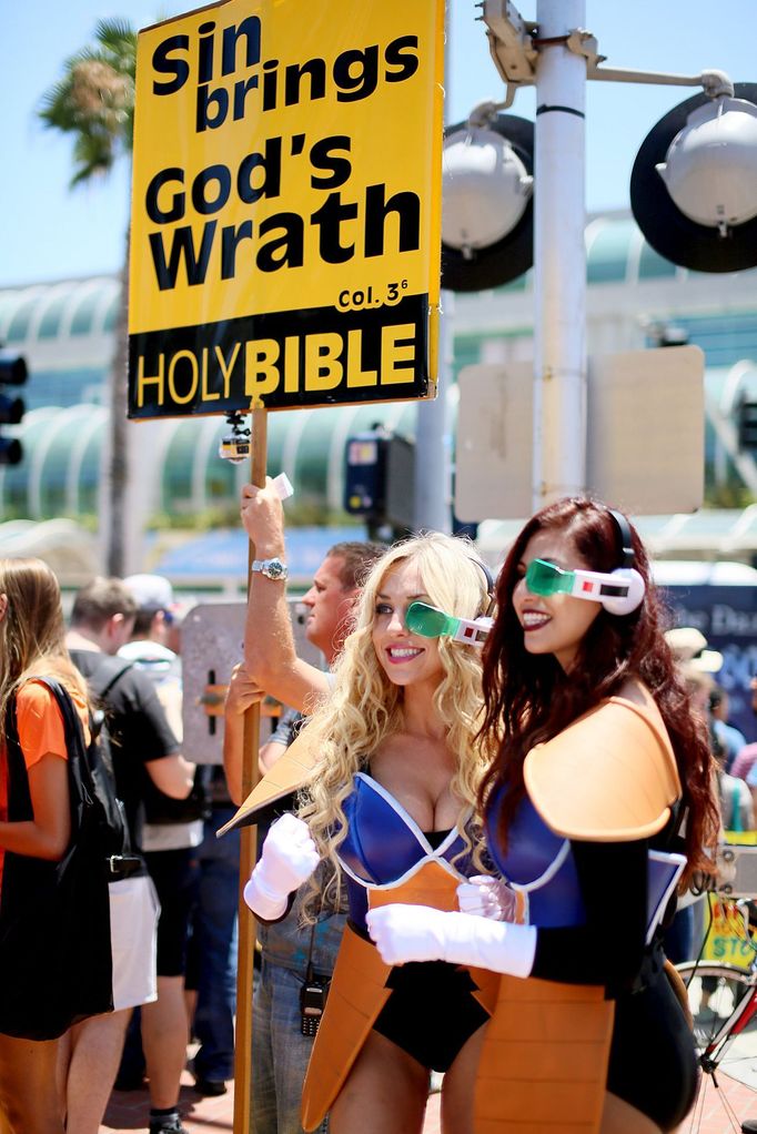 Cosplayers pose for pictures while a picketer holds a pro-religion sign outside of the Convention Center at the 2015 Comic-Con International in San Diego