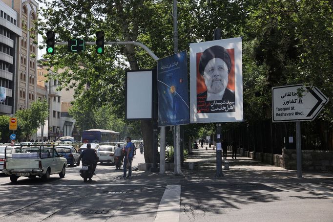 Lidé projíždějí kolem transparentu s fotografií zesnulého íránského prezidenta Ebrahima Raisiho na ulici v Teheránu.