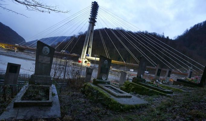 A graveyard is seen next to a bridge for the new highway connecting Sochi, the host city for the Sochi 2014 Winter Olympics, and the winter sport resort of Krasnaya Polyana, February 18, 2013. Although many complexes and venues in the Black Sea resort of Sochi mostly resemble building sites that are still under construction, there is nothing to suggest any concern over readiness. Construction will be completed by August 2013 according to organizers. The Sochi 2014 Winter Olympics opens on February 7, 2014. REUTERS/Kai Pfaffenbach (RUSSIA - Tags: BUSINESS CONSTRUCTION CITYSCAPE ENVIRONMENT SPORT OLYMPICS) Published: Úno. 18, 2013, 7:26 odp.