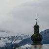 A spire is displayed in front of fields with light dusting of snow in the western Austrian village of Tulfes
