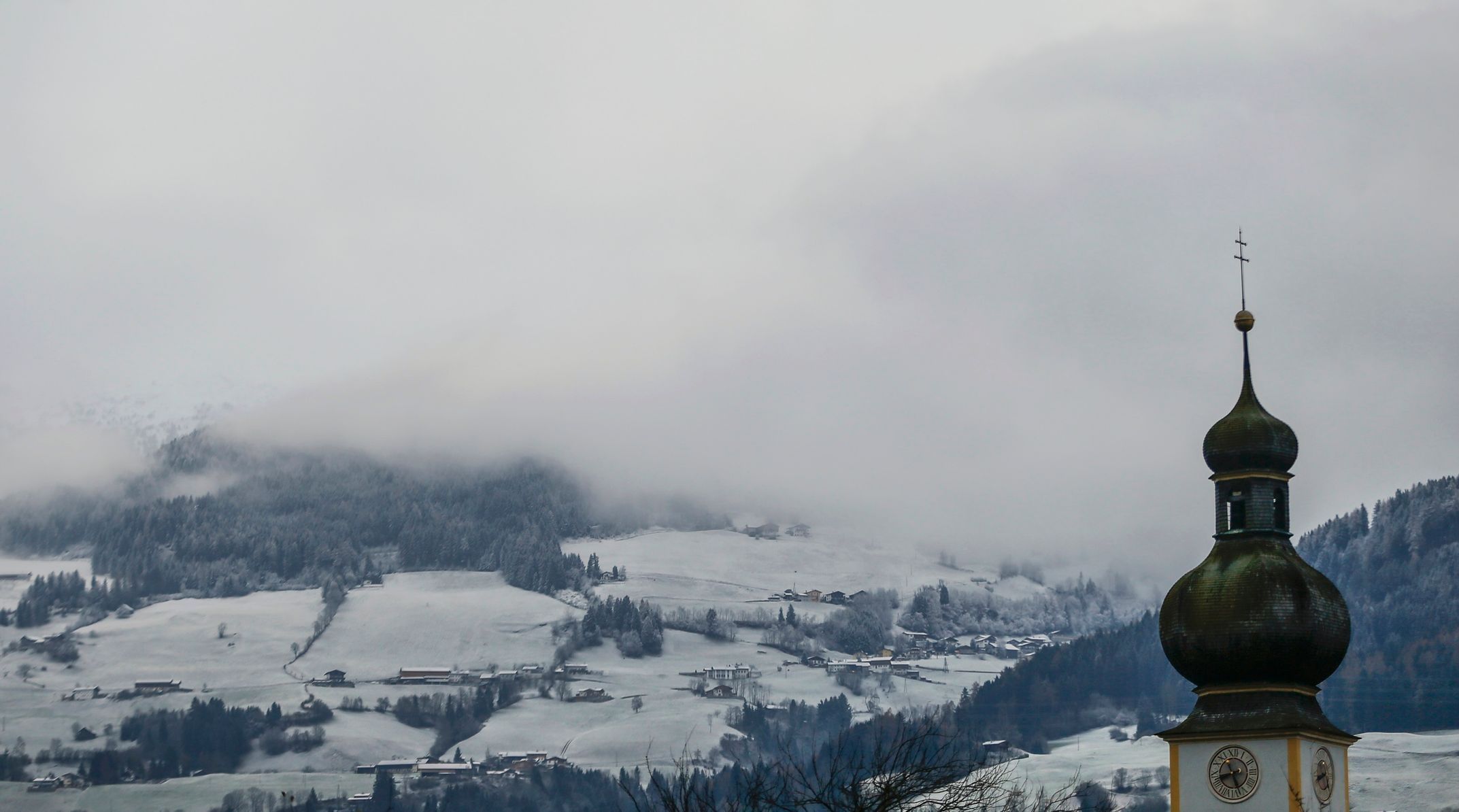 A spire is displayed in front of fields with light dusting of snow in the western Austrian village of Tulfes