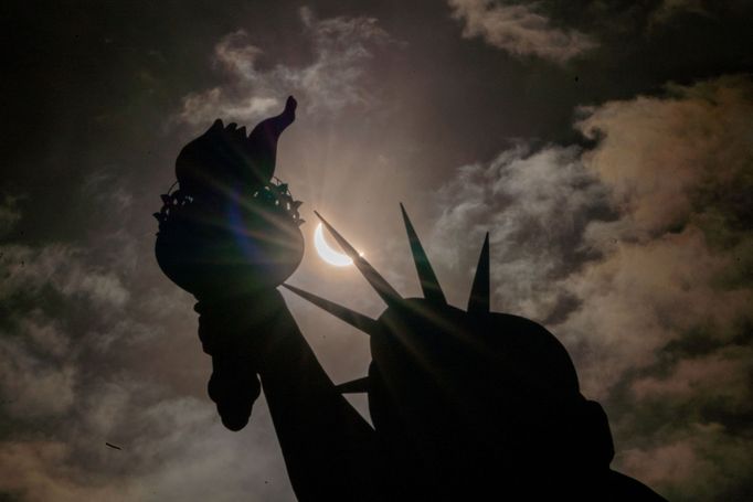 Socha Svobody při částečném zatmění Slunce, kdy Měsíc částečně zakrývá Slunce, na ostrově Liberty Island v New Yorku.