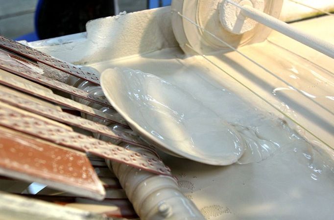 Porcelánový talířek vyjíždí z glazurové lázně. Na výrobu tvrdého porcelánu se používá 50% kaolinu, 25% křemene a 25% živce. Někdy se přidává také křída a mramor.