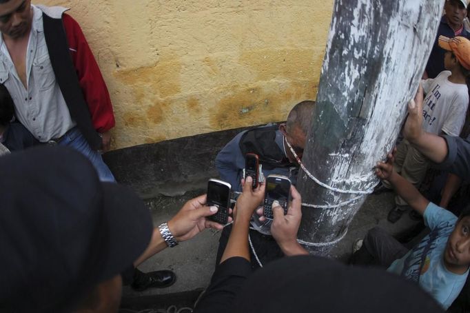 Police officers take a picture with their cellphones of man who is tied up and beaten by villagers, after he was accused of theft, at Tactic, in Alta Verapaz region, about 189km (117 miles) from Guatemala City, September 13, 2012. The local community tied up and beat four men who were accused of theft in the aftermath of a school killing, which had occurred on Wednesday. The man, who had entered a classroom and killed two children, ages 8 and 13, with a machete, was lynched and burnt alive by a mob, local media reported. REUTERS/Jorge Dan Lopez (GUATEMALA - Tags: CRIME LAW SOCIETY) Published: Zář. 13, 2012, 6:12 odp.