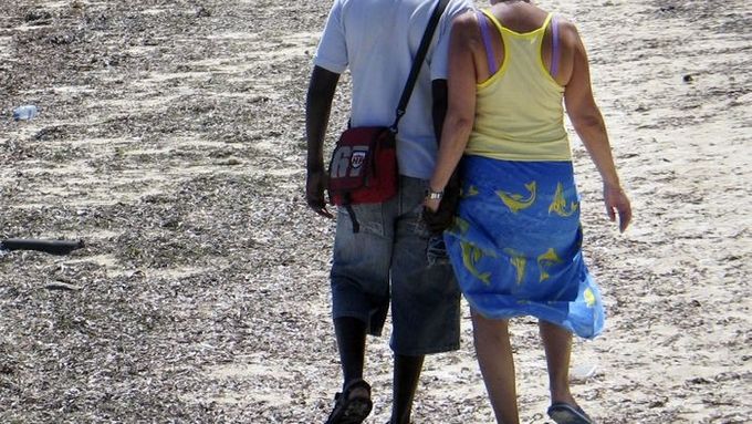 Mladý Afričan se prochází po pláži ruku v ruce se svou  o desítky let starší přítelkyní ze západní Evropy