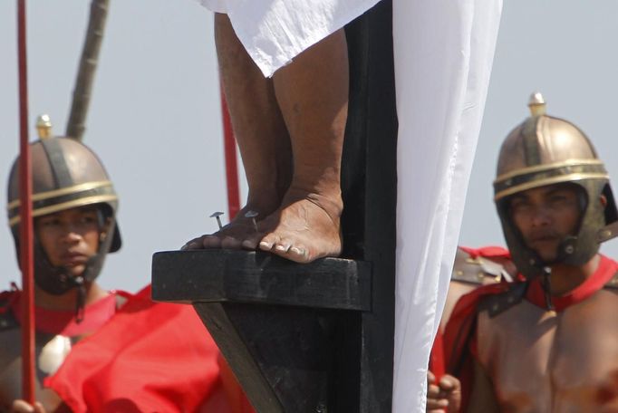 Ruben Enaje, 52, who is portraying Jesus Christ for the 27th time, is closely watched by two men who play Roman soldiers while his feet are nailed to a wooden cross during a Good Friday crucifixion re-enactment in San Pedro Cutud town, Pampanga province, north of Manila March 29, 2013. The Roman Catholic church frowns on the gory spectacle held in the Philippine village of Cutud every Good Friday but does nothing to deter the faithful from emulating the suffering of Christ and taking a painful route to penitence. Holy Week is celebrated in many Christian traditions during the week before Easter. REUTERS/Romeo Ranoco (PHILIPPINES - Tags: RELIGION SOCIETY) Published: Bře. 29, 2013, 8:11 dop.