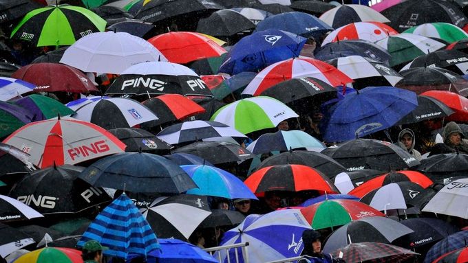 Návštěvníci golfového turnaje British Open se schovávají pod deštníky, zatímco sledují hru u osmnácté jamky. Jižní Anglie, hřiště Royal St George's v Sandwichi.
