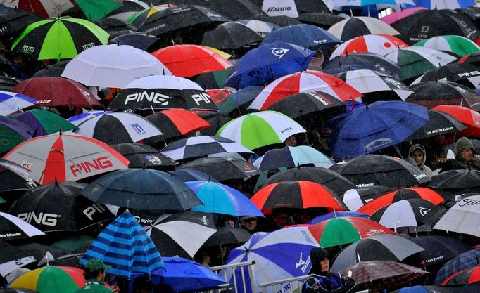 Návštěvníci golfového turnaje British Open se schovávají pod deštníky, zatímco sledují hru u osmnácté jamky. Jižní Anglie, hřiště Royal St George's v Sandwichi.