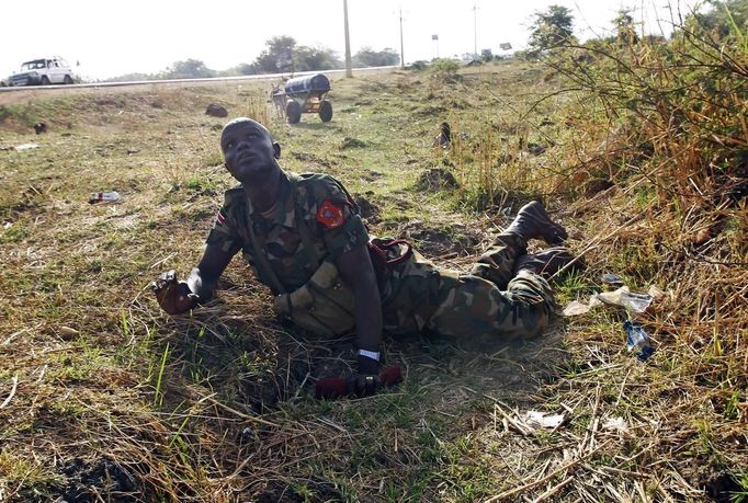 A SPLA soldier looks at warplanes as he lies on the ground to take cover beside a road during an air strike in Rubkona