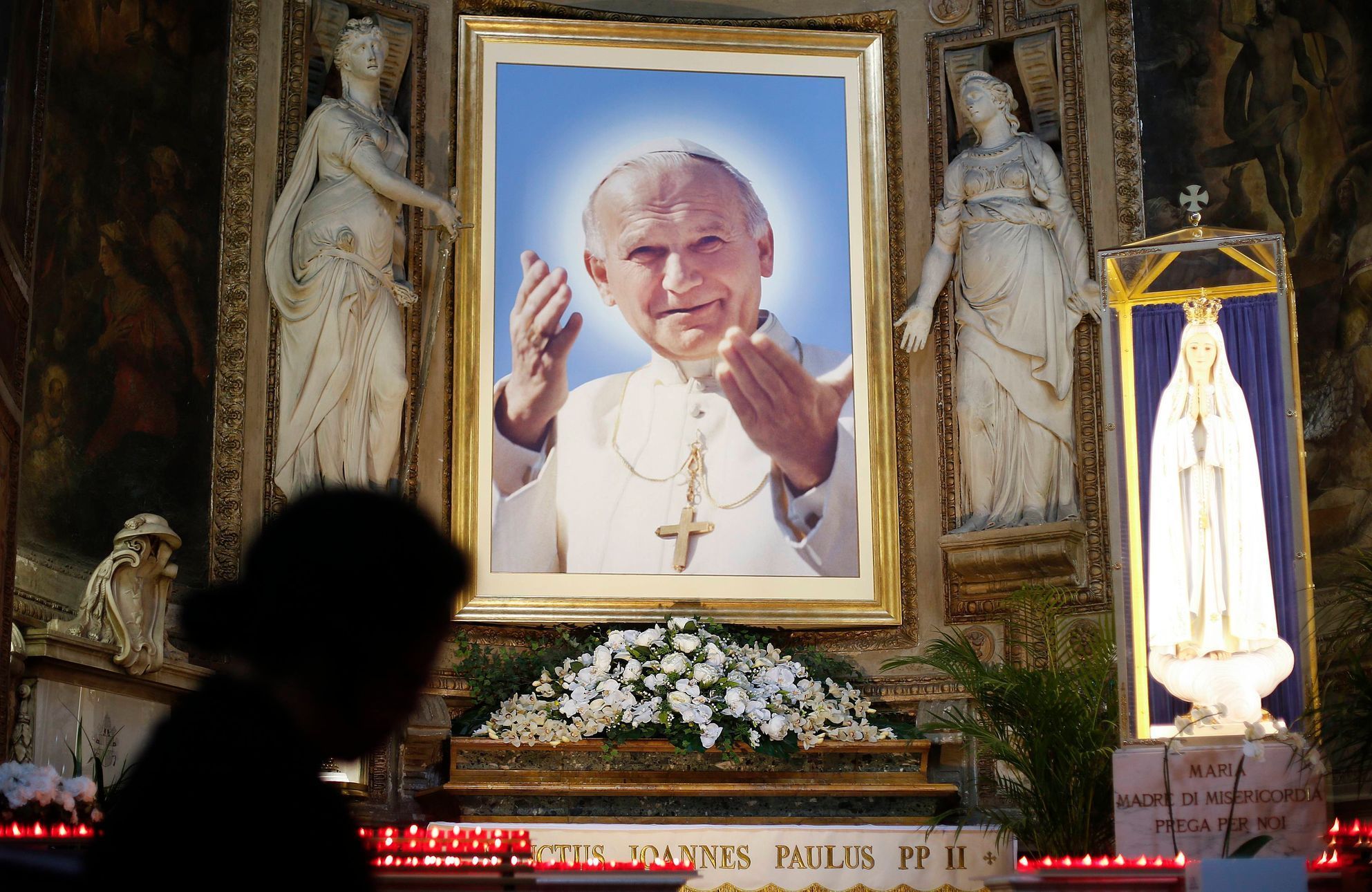 A woman prays in front of a painting depicting Pope John Paul II in a church in downtown Rome