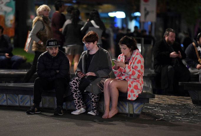 People evacuated from buildings along Dixon Street check their mobile phones while sitting on a bench in Wellington.