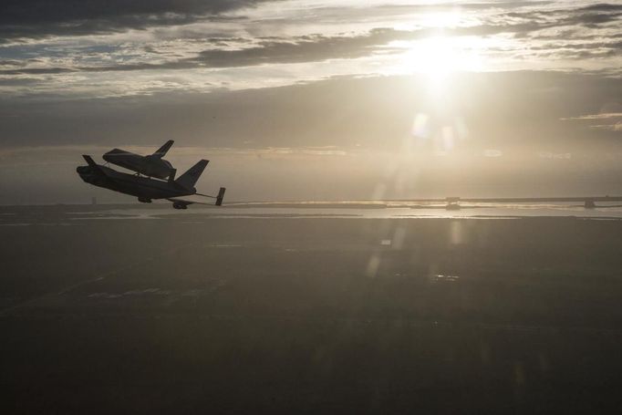 The space shuttle Endeavour, atop NASA's Shuttle Carrier Aircraft, flies over the Kennedy Space Center in Cape Canaveral, Florida in the early morning light in this September 19, 2012 NASA handout photo. The SCA, a modified 747 jetliner is flying Endeavour to Los Angeles where it will be placed on public display at the California Science Center. This is the final ferry flight scheduled in the Space Shuttle Program era. REUTERS/Robert Markowitz/NASA/Handout. (UNITED STATES - Tags: SCIENCE TECHNOLOGY TRANSPORT) THIS IMAGE HAS BEEN SUPPLIED BY A THIRD PARTY. IT IS DISTRIBUTED, EXACTLY AS RECEIVED BY REUTERS, AS A SERVICE TO CLIENTS. FOR EDITORIAL USE ONLY. NOT FOR SALE FOR MARKETING OR ADVERTISING CAMPAIGNS Published: Zář. 20, 2012, 1:55 dop.