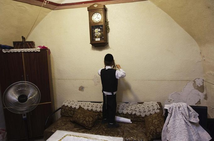 Haim Kreus, 6, hangs a decoration on the wall during his family's preparations for the Jewish Sabbath in Jerusalem's Mea Shearim neighbourhood June 29, 2012. The Kreus family are a member of Neturei Karta, a fringe ultra-Orthodox movement within the anti-Zionist bloc. The ultra-Orthodox Jews have gone from being a tiny minority in Israel's mostly secular society to its fastest-growing sector, now about 10 percent of the 7.8 million population. They are exempt from military duty in Israel but draft deferments and state subsidies for the ultra-Orthodox have become a divisive political issue in Israel, where the government must decide a new law by August to ensure more of them do military service. Picture taken June 29, 2012. REUTERS/Ronen Zvulun (JERUSALEM - Tags: RELIGION POLITICS MILITARY) ATTENTION EDITORS - PICTURE 6 OF 21 FOR PACKAGE "ISRAEL'S ULTRA-ORTHODOX". SEARCH "ULTRA-ORTHODOX" FOR ALL PICTURES Published: Čec. 6, 2012, 10 dop.