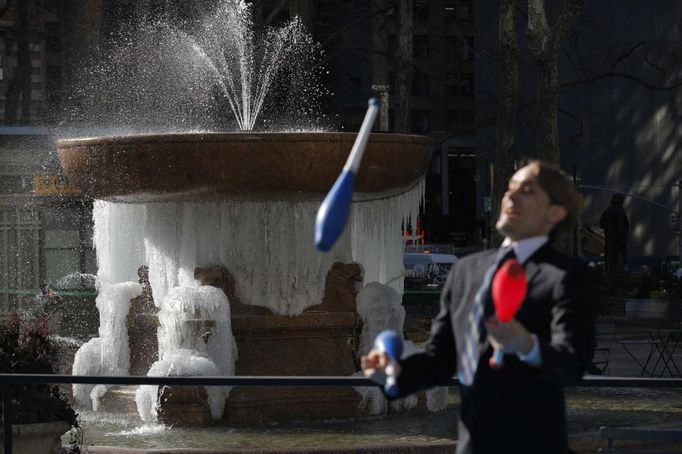 A man juggles while a fountain that is partially frozen into ice is seen in the background at Bryant Park in New York, January 24, 2013. Frigid arctic air held the U.S. Midwest and Northeast in its icy grip on Wednesday, with the cold so dangerous that municipal emergency warming centers opened up and ski resorts shut down. Wintry conditions from Minneapolis to Washington marked the coldest conditions in many parts of the United States in four years, but were nowhere near the record lows for January, meteorologists said. REUTERS/Eduardo Munoz (UNITED STATES - Tags: ENVIRONMENT SOCIETY) Published: Led. 24, 2013, 7:29 odp.