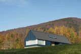 Dům s bílými okenicemi a modrými palubkami evokuje charakter přímořské vesnice nebo skalnatého pobřeží Skandinávie. Nová dřevostavba ale stojí mnohem blíž.