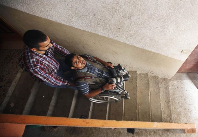 Wheelchair-bound Palestinian freelance photographer Moamen Qreiqea is helped by his brother at his home in Gaza City October 1, 2012. Qreiqea, 25, lost both his legs in an Israeli air strike in 2008 while taking pictures east of Gaza. The father of two is determined to continue his career despite his disability. REUTERS/Suhaib Salem (GAZA - Tags: MEDIA SOCIETY) Published: Říj. 1, 2012, 3:39 odp.