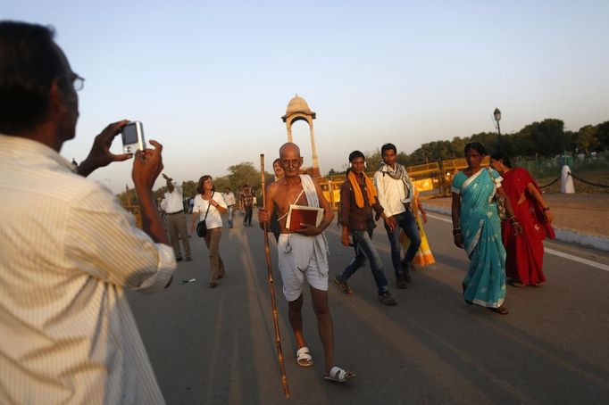 A man takes a photo as Mahesh Chaturvedi (C), 63, who dresses up like Mahatma Gandhi, walks near the India Gate in New Delhi October 4, 2012. Chaturvedi says that the soul of Gandhi resides in him and he has been sent to continue the work of Father of the Nation. After his self proclaimed transformation in 2002 as Gandhi, Chaturvedi has been travelling extensively and plays up to his startling resemblance to Gandhi at protests and demonstrations. Picture taken October 4, 2012. REUTERS/Mansi Thapliyal (INDIA - Tags: SOCIETY) Published: Lis. 26, 2012, 4 dop.